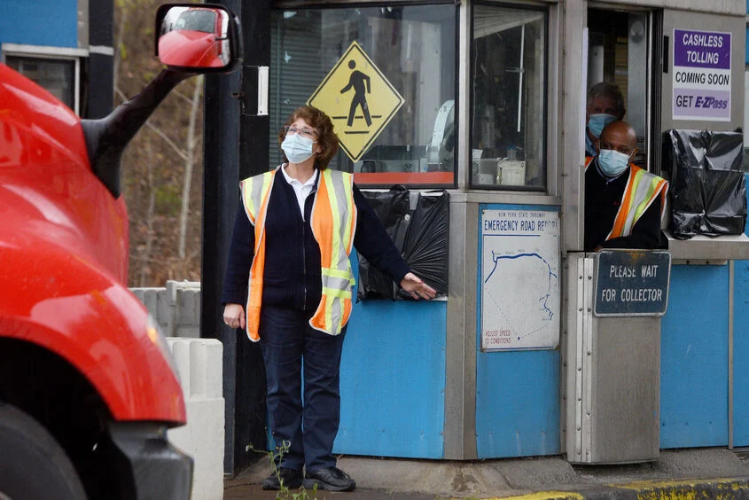 two ticket toll booth attendants directing a truck to pass wearing face masks clean air needed